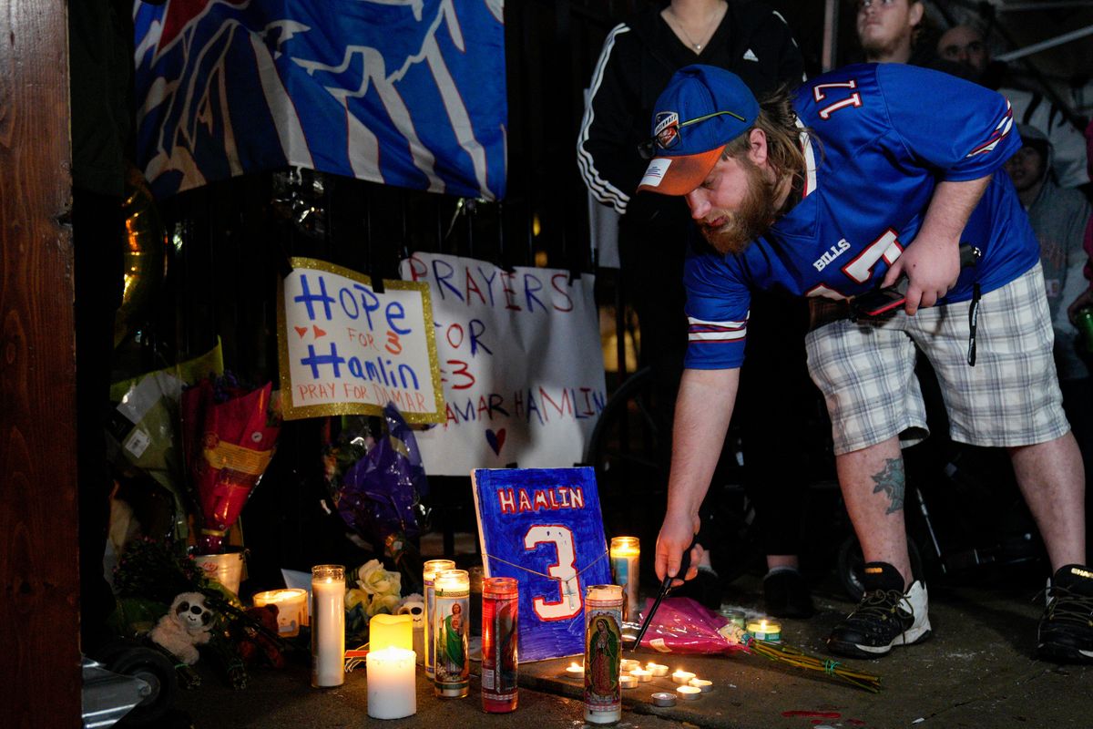 A well-wisher lights a candle at a makeshift tribute to the critically injured Bills defensive back.