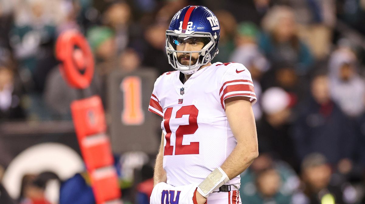 A white man in a white NY Giants red, white, and blue inform and blue helmet stands with his hands in a warmer during an NFL football game.