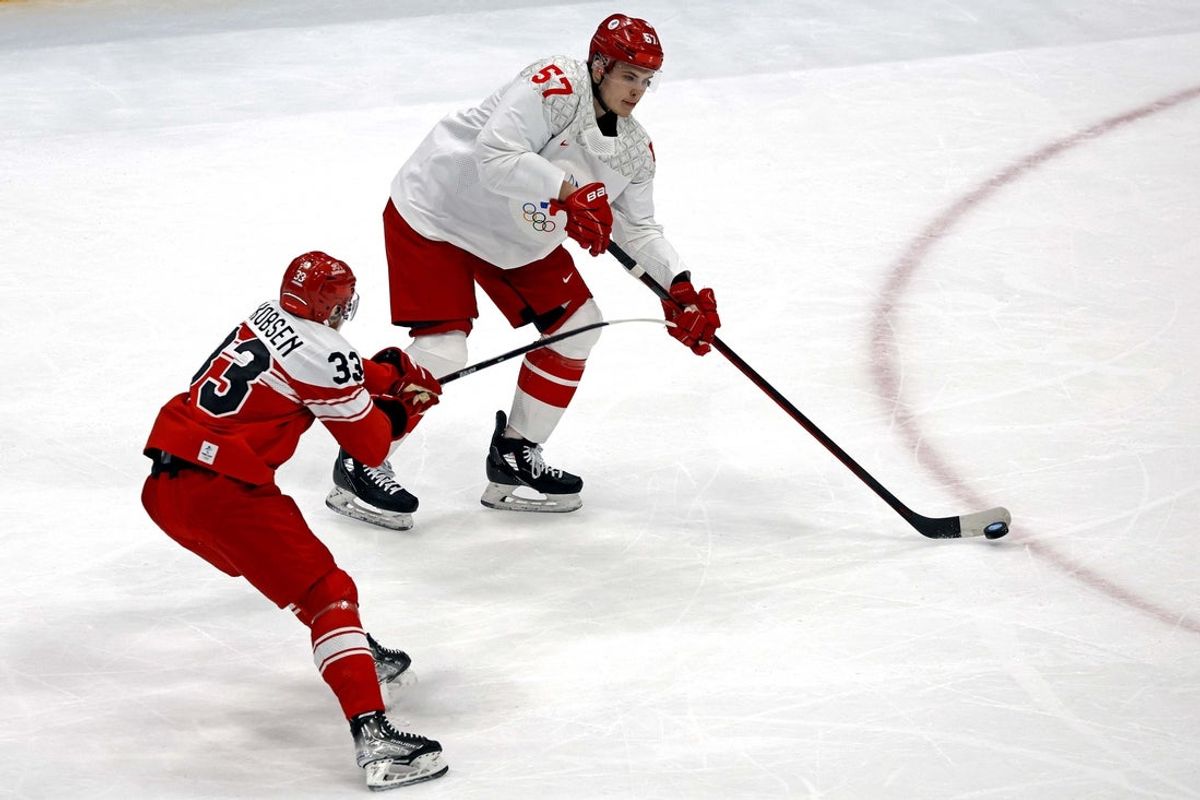 Feb 11, 2022; Beijing, China;  ROC defender Alexander Nikishin (57) passes the puck against  Denmark forward Julian Jakobsen (33) in men's ice hockey Group B play during the Beijing 2022 Olympic Winter Games at National Indoor Stadium. Mandatory Credit: Peter Casey-Imagn Images