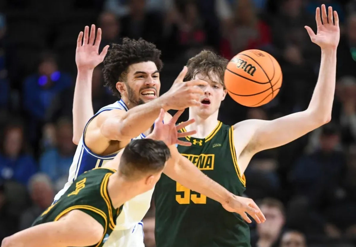 El escolta de los Siena Saints, Gavin Doty (4), y el pívot de los Siena Saints, Riley Mulvey (55), defienden al alero de los Duke Blue Devils, Cameron Boozer (12), el jueves 19 de marzo de 2026, durante el partido de primera ronda del Torneo de Baloncesto Masculino de la NCAA en el Bon Secours Wellness Arena en Greenville, Carolina del Sur. Los Duke Blue Devils ganaron 71-65.