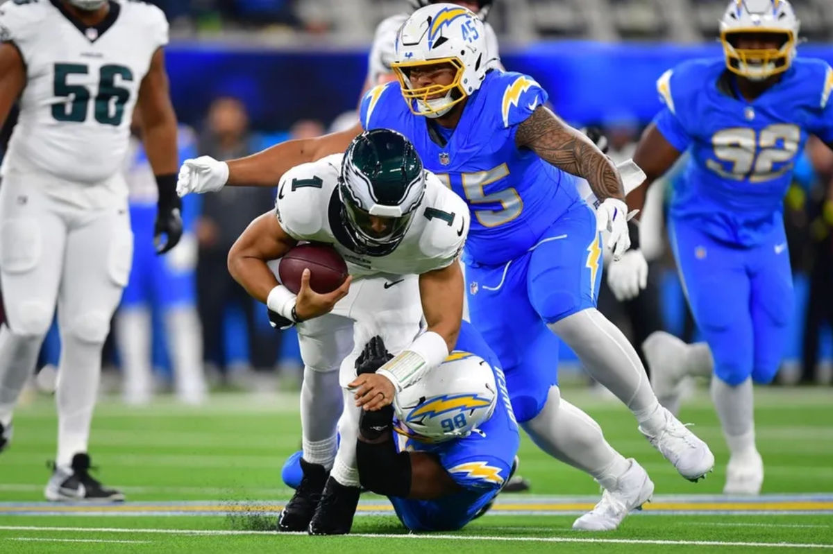 8 de dezembro de 2025; Inglewood, Califórnia, EUA; O linebacker do Los Angeles Chargers, Odafe Oweh (98), derruba o quarterback do Philadelphia Eagles, Jalen Hurts (1), no primeiro tempo no SoFi Stadium. Crédito obrigatório: Gary A. Vasquez-Imagn Images