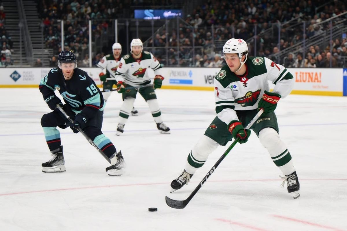 Dec 10, 2023; Seattle, Washington, USA; Minnesota Wild defenseman Brock Faber (7) plays the puck while defended by Seattle Kraken left wing Jared McCann (19) during the third period at Climate Pledge Arena.