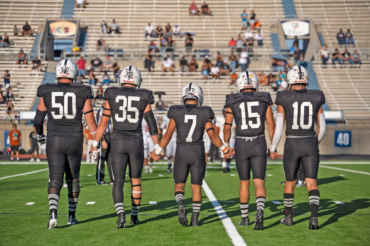 Permian players hold hands on way to coin toss before start of a day game.