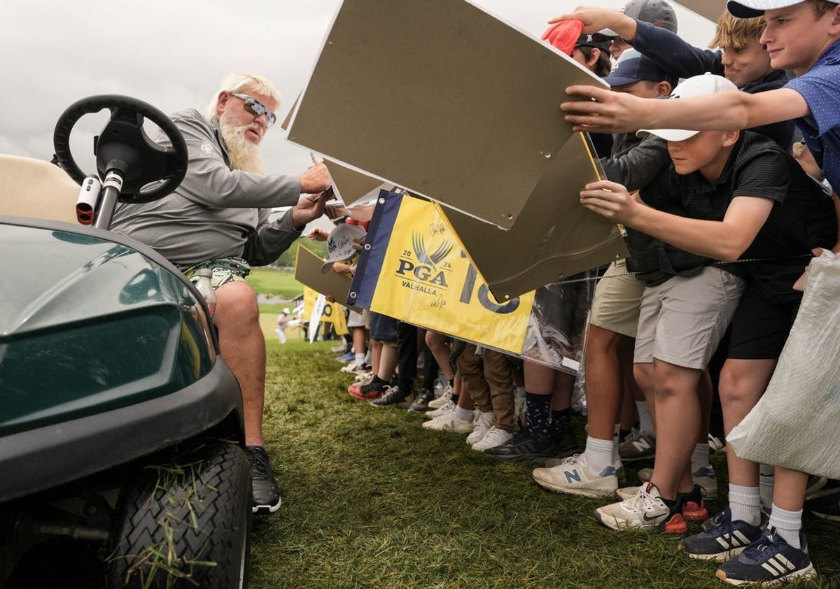 John Daly signs autographs for spectators while driving his golf cart outside the 18th green at the 2024 PGA Championship Wednesday practice at Valhalla Golf Course in Louisville, Kentucky. May 15, 2024.