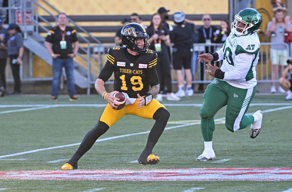 Jun 16, 2024; Hamilton, Ontario, CAN; Hamilton Tiger Cats quarterback Bo Levi Mitchell (19) is pursued by Saskatchewan Rough Riders defensive lineman Miles Brown (90) at Tim Hortons Field. Mandatory Credit: Gerry Angus-USA TODAY Sports