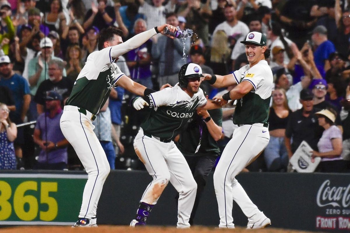 Jun 22, 2024; Denver, Colorado, USA;  Colorado Rockies third base Ryan McMahon (24) is doused by outfielder Nolan Jones (22) as Rockies first base Michael Toglia (4) looks on after McMahon drew the game winning walk due to a pitch timer violation in the ninth inning against the Washington Nationals at Coors Field. Mandatory Credit: John Leyba-USA TODAY Sports