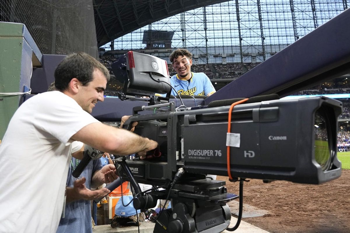 Jun 28, 2024; Milwaukee, Wisconsin, USA;  Milwaukee Brewers shortstop Willy Adames (27) looks on while a technician repairs a TV camera in the first base photo well during the third inning against the Chicago Cubs at American Family Field. Mandatory Credit: Jeff Hanisch-Imagn Images