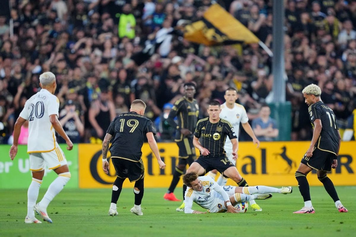 Jul 4, 2024; Pasadena, California, USA; LA Galaxy midfielder Riqui Puig (10) reacts while falling to the pitch as LAFC defender Sergi Palencia (14) looks on during the first half at Rose Bowl. Mandatory Credit: Kirby Lee-USA TODAY Sports
