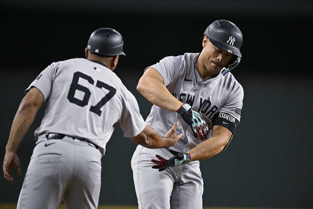 Sep 2, 2024; Arlington, Texas, USA; New York Yankees third base coach Luis Rojas (67) pretends to hand off a football to designated hitter Giancarlo Stanton (27) after Stanton hits a home run against the Texas Rangers during the eighth inning at Globe Life Field. Mandatory Credit: Jerome Miron-USA TODAY Sports