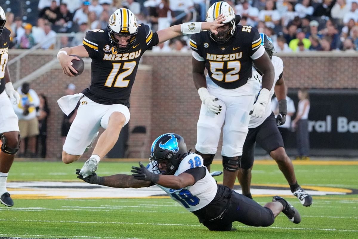 Sep 7, 2024; Columbia, Missouri, USA; Missouri Tigers quarterback Brady Cook (12) leaps over Buffalo Bulls linebacker Dion Crawford (18) and runs in for a touchdown during the first half at Faurot Field at Memorial Stadium. Mandatory Credit: Denny Medley-Imagn Images