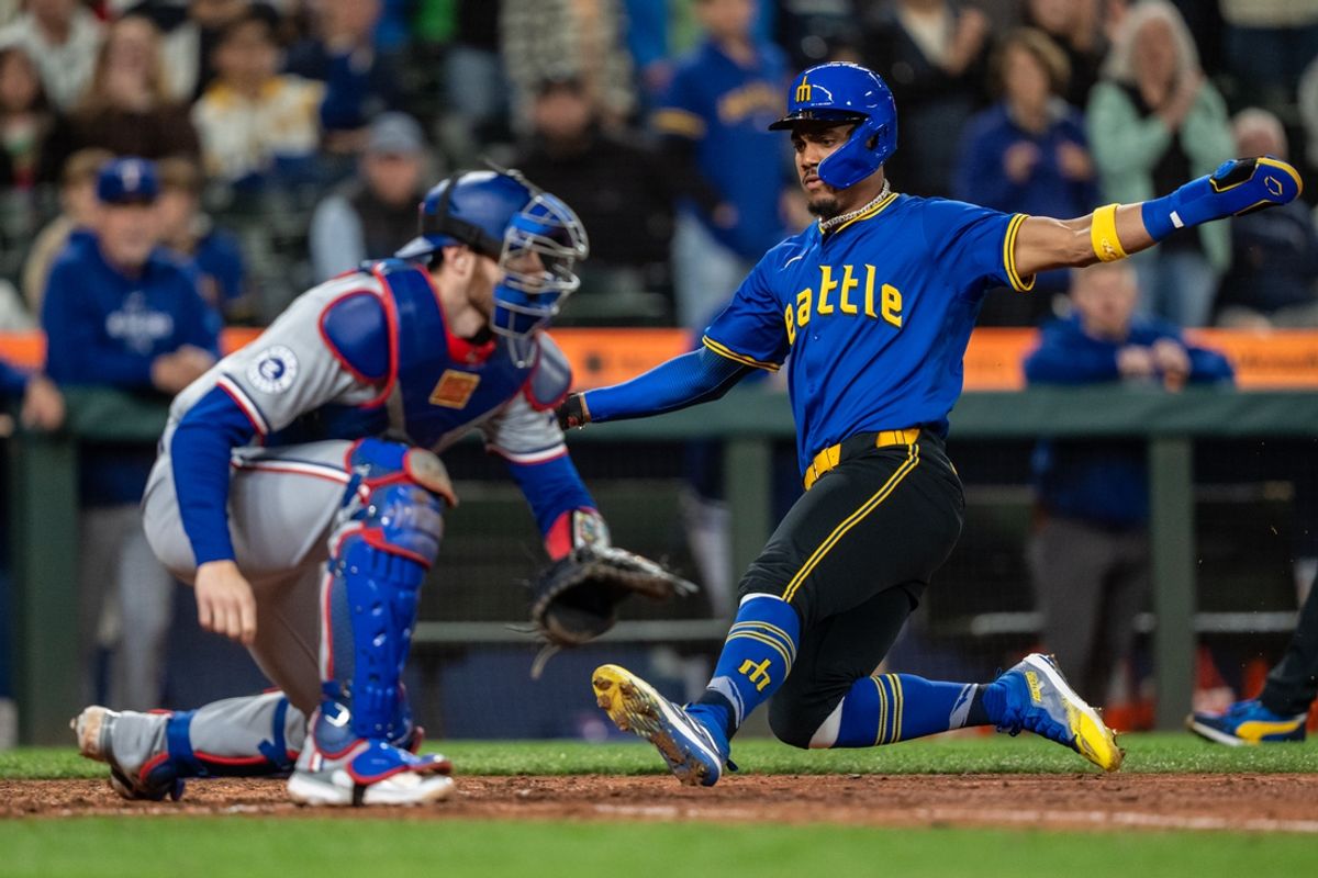 Sep 13, 2024; Seattle, Washington, USA;  Seattle Mariners centerfielder Julio Rodriguez (44) slides safely into home plate to score a run ahead of a tag by Texas Rangers catcher Jonah Heim (28) during the seventh inning at T-Mobile Park. Mandatory Credit: Stephen Brashear-Imagn Images