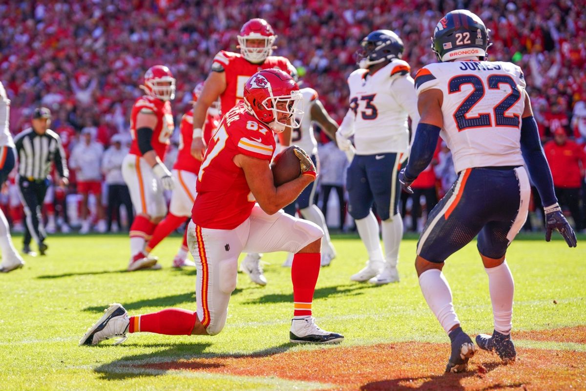 Nov 10, 2024; Kansas City, Missouri, USA; Kansas City Chiefs tight end Travis Kelce (87) scores a touchdown as Denver Broncos safety Brandon Jones (22) looks on  during the first half at GEHA Field at Arrowhead Stadium. Mandatory Credit: Denny Medley-Imagn Images