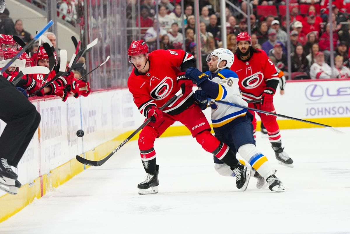 Nov 17, 2024; Raleigh, North Carolina, USA;  St. Louis Blues left wing Nathan Walker (26) checks Carolina Hurricanes center Martin Necas (88) during the first period at Lenovo Center. Mandatory Credit: James Guillory-Imagn Images