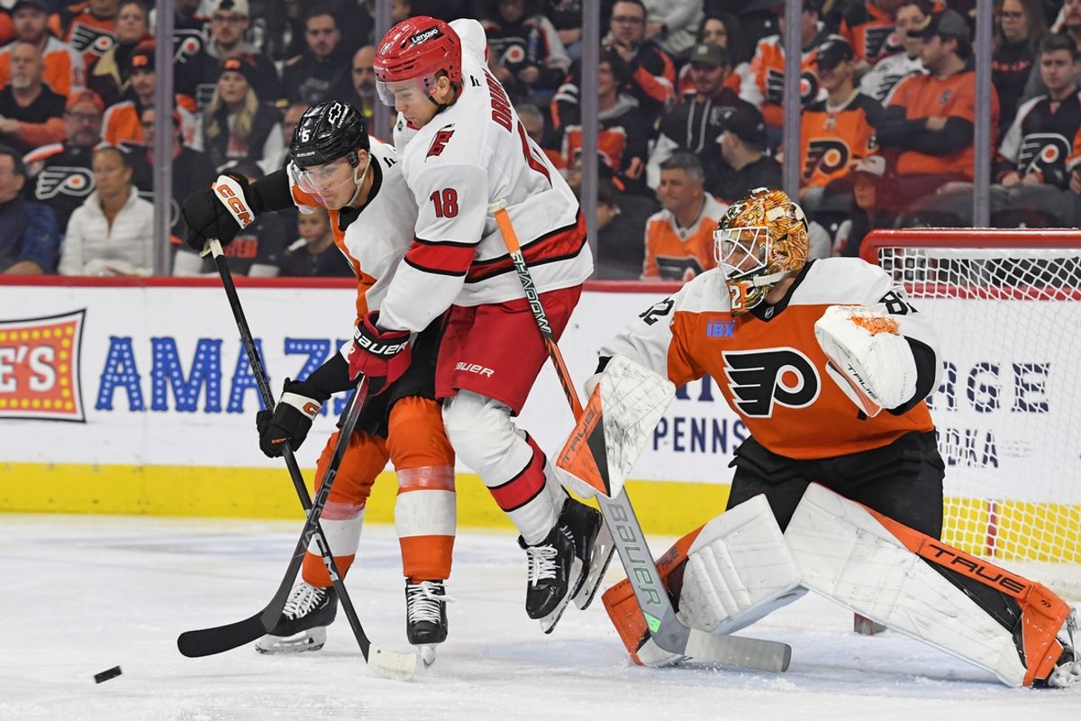 Nov 20, 2024; Philadelphia, Pennsylvania, USA; Carolina Hurricanes center Jack Drury (18) and Philadelphia Flyers defenseman Egor Zamula (5) battle for the puck in front of goaltender Ivan Fedotov (82) during the first period at Wells Fargo Center. Mandatory Credit: Eric Hartline-Imagn Images