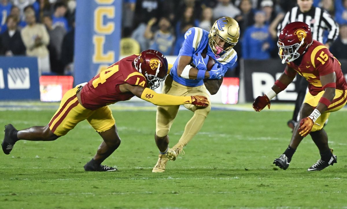 Nov 23, 2024; Pasadena, California, USA; UCLA Bruins wide receiver Titus Mokiao-Atimalala (2) tries to run past USC Trojans cornerback Jacobe Covington (14) and safety Anthony Beavers Jr. (15) during the first quarter at Rose Bowl. Mandatory Credit: Robert Hanashiro-Imagn Images