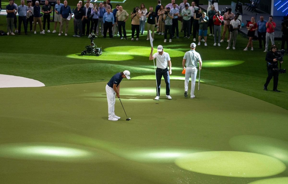 Billy Horschel holds the flag for Rickie Fowler as he puts next to Wyndham Clark, right, during media day at the SoFi Center, the home of TGL, the interactive golf league founded by Tiger Woods and Rory McIlroy on December 18, 2024, in Palm Beach Gardens, Florida.