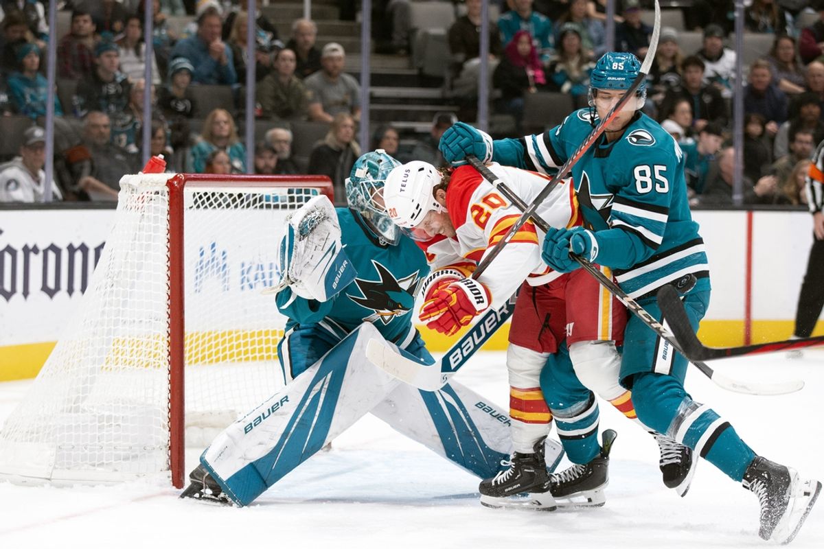 Dec 28, 2024; San Jose, California, USA; San Jose Sharks defenseman Shakir Mukhamadullin (85) ties up Calgary Flames center Blake Coleman (20) in front of goaltender Yaroslav Askarov (30) during the first period at SAP Center at San Jose. Mandatory Credit: D. Ross Cameron-Imagn Images