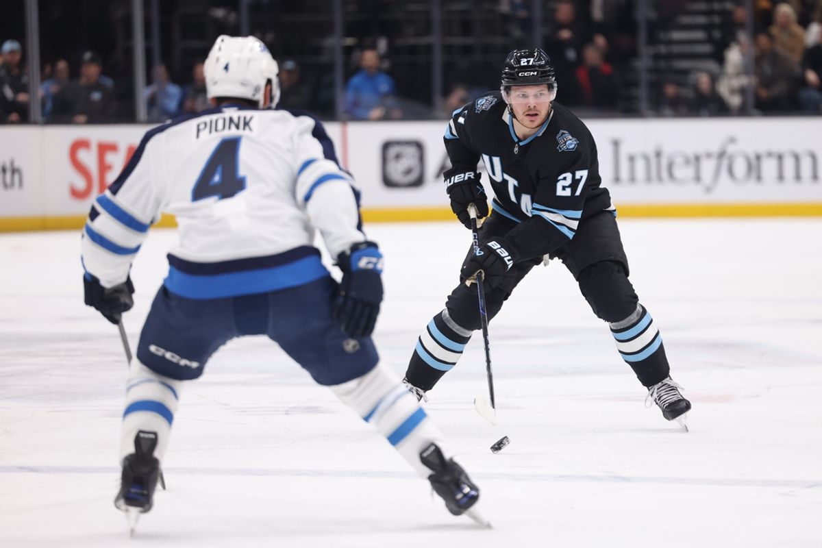 Jan 20, 2025; Salt Lake City, Utah, USA; Utah Hockey Club center Barrett Hayton (27) skates with the puck against Winnipeg Jets defenseman Neal Pionk (4) during the second period at Delta Center. Mandatory Credit: Rob Gray-Imagn Images