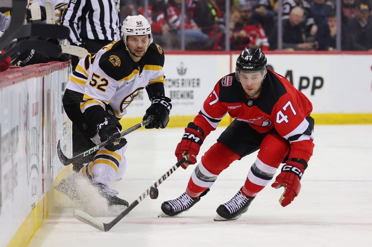 Jan 22, 2025; Newark, New Jersey, USA; Boston Bruins defenseman Andrew Peeke (52) plays the puck while being defended by New Jersey Devils center Paul Cotter (47) during the first period at Prudential Center. Mandatory Credit: Ed Mulholland-Imagn Images