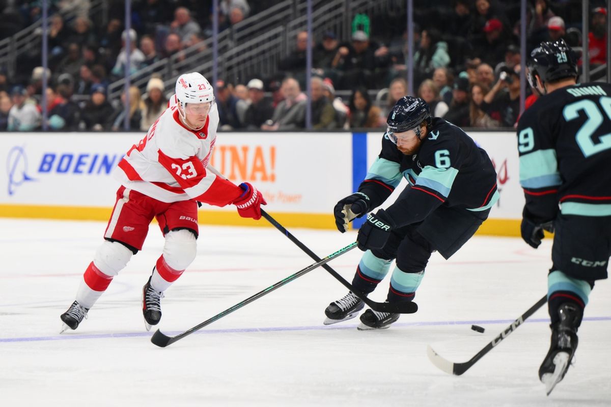 Feb 4, 2025; Seattle, Washington, USA; Detroit Red Wings left wing Lucas Raymond (23) passes the puck past Seattle Kraken defenseman Adam Larsson (6) during the third period at Climate Pledge Arena. Mandatory Credit: Steven Bisig-Imagn Images