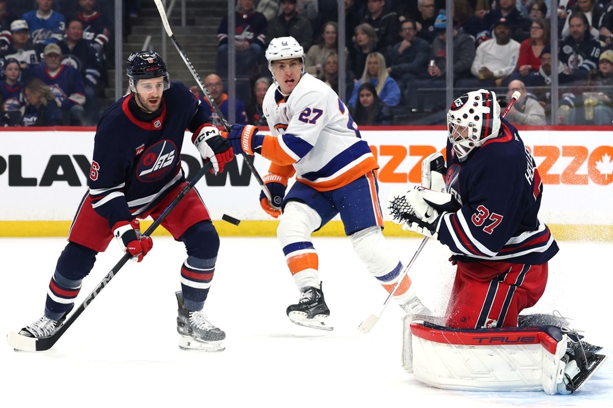 Feb 7, 2025; Winnipeg, Manitoba, CAN; Winnipeg Jets defenseman Colin Miller (6) and New York Islanders center Brock Nelson (29) eye an incoming shot on Winnipeg Jets goaltender Connor Hellebuyck (37) in the first period at Canada Life Centre. Mandatory Credit: James Carey Lauder-Imagn Images