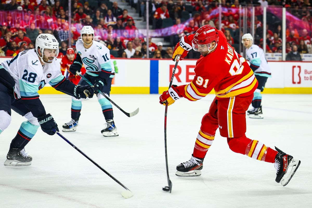 Feb 8, 2025; Calgary, Alberta, CAN; Calgary Flames center Nazem Kadri (91) shoots the puck as Seattle Kraken defenseman Joshua Mahura (28) defends during the second period at Scotiabank Saddledome. Mandatory Credit: Sergei Belski-Imagn Images