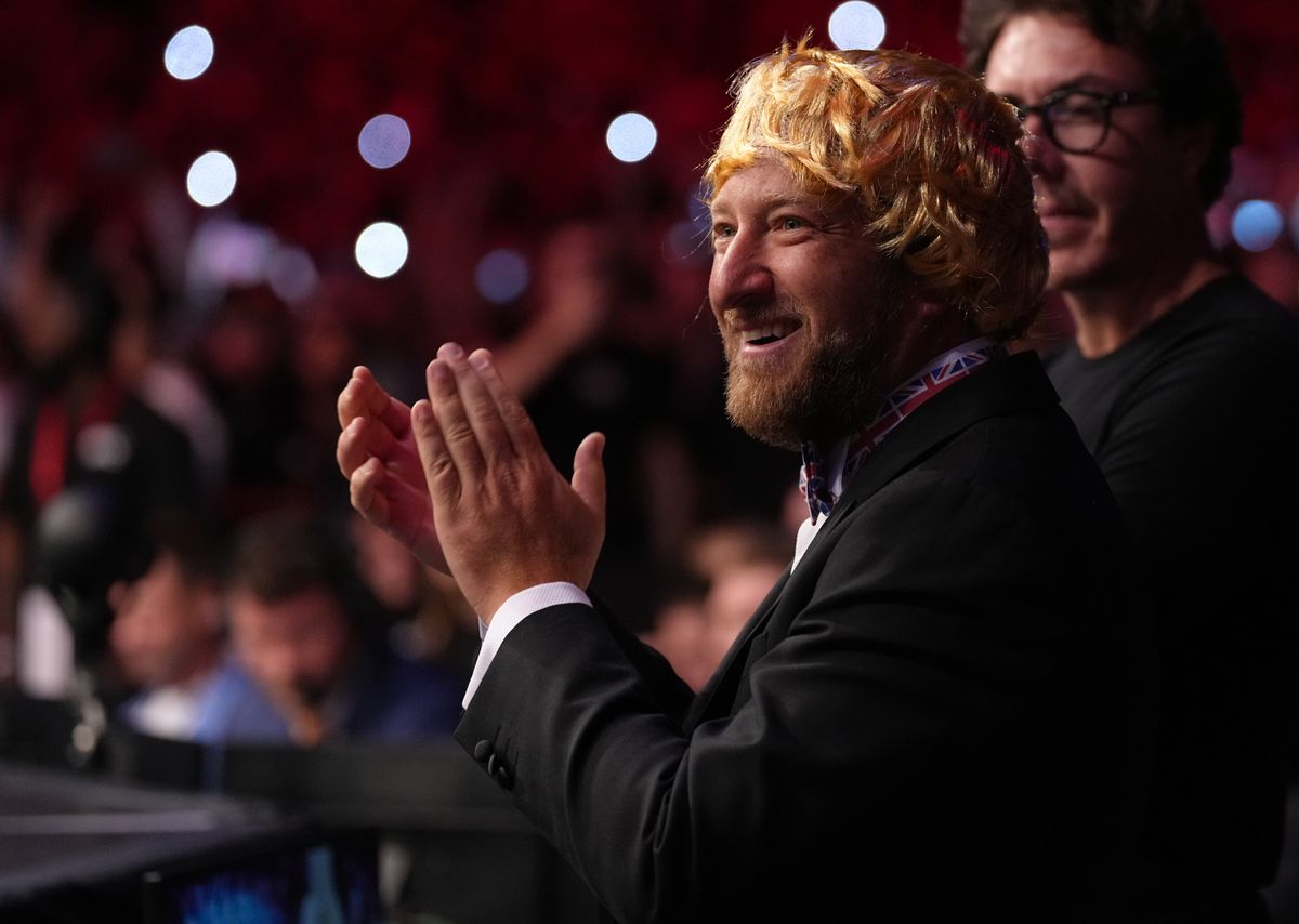 A dumb-looking white man with a yellow wig on his head claps wildly.