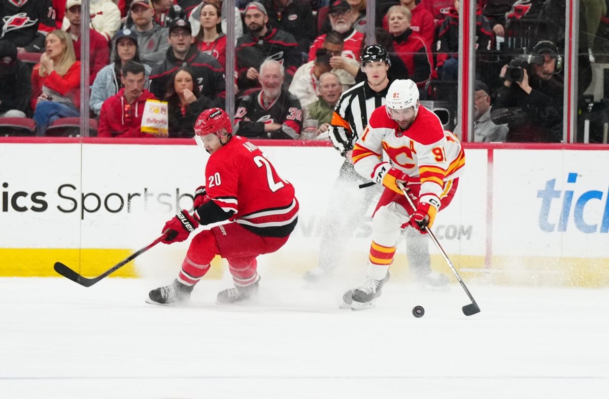 Mar 2, 2025; Raleigh, North Carolina, USA; Calgary Flames center Nazem Kadri (91) skates with the puck inside of Carolina Hurricanes center Sebastian Aho (20) during the first period at Lenovo Center. Mandatory Credit: James Guillory-Imagn Images