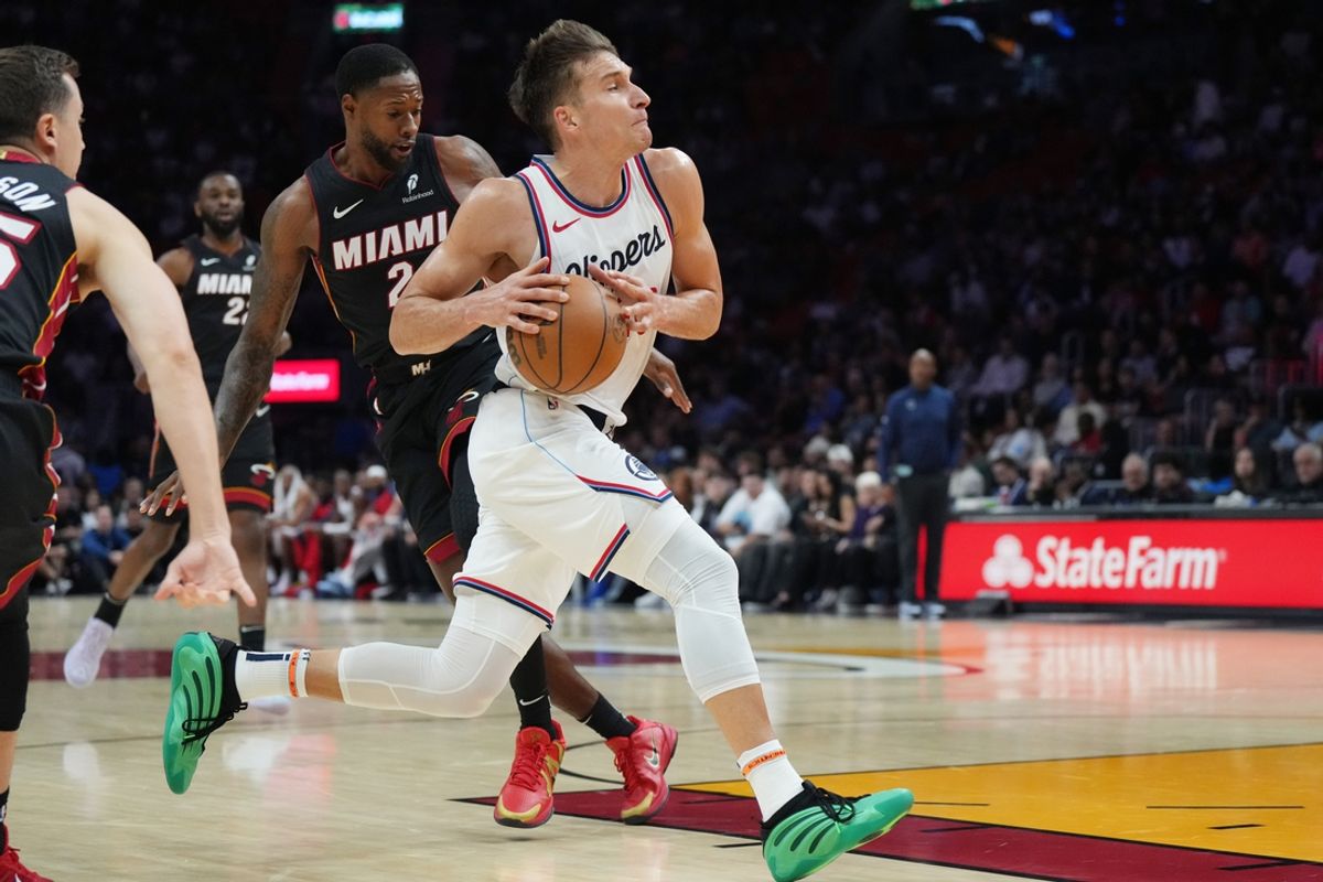 Mar 12, 2025; Miami, Florida, USA;  LA Clippers guard Bogdan Bogdanovic (10) splits the defense of Miami Heat forward Duncan Robinson (55) and forward Haywood Highsmith (24) during the first half at Kaseya Center. Mandatory Credit: Jim Rassol-Imagn Images