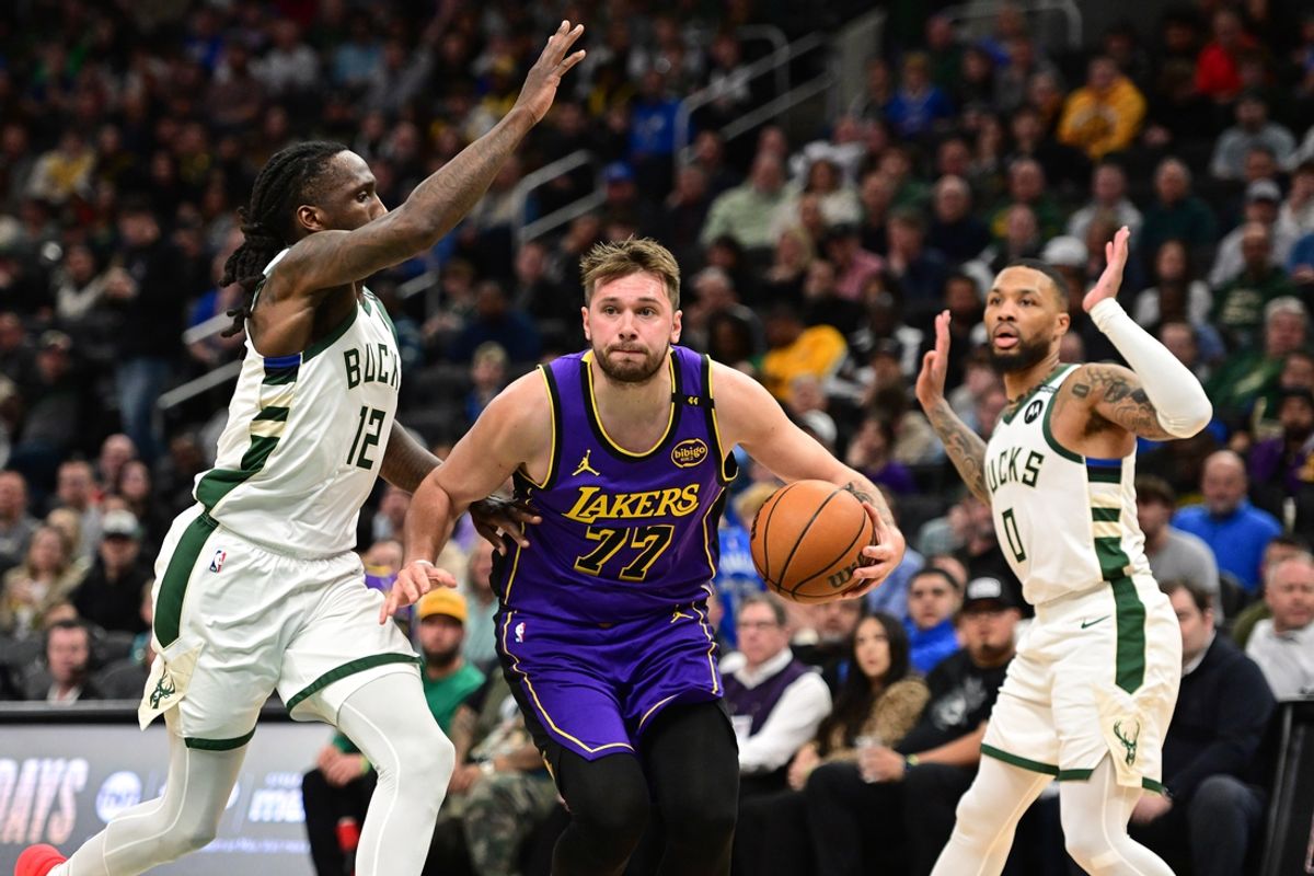 Mar 13, 2025; Milwaukee, Wisconsin, USA; Los Angeles Lakers guard Luka Doncic (77) drives to the basket between Milwaukee Bucks guard Taurean Prince (12) and guard Damian Lillard (0) in the third quarter at Fiserv Forum. Mandatory Credit: Benny Sieu-Imagn Images