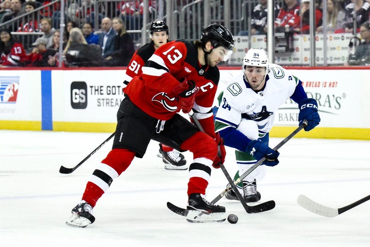 Mar 24, 2025; Newark, New Jersey, USA; New Jersey Devils center Nico Hischier (13) skates with the puck while being defended by Vancouver Canucks center Linus Karlsson (94) during the first period at Prudential Center. Mandatory Credit: John Jones-Imagn Images