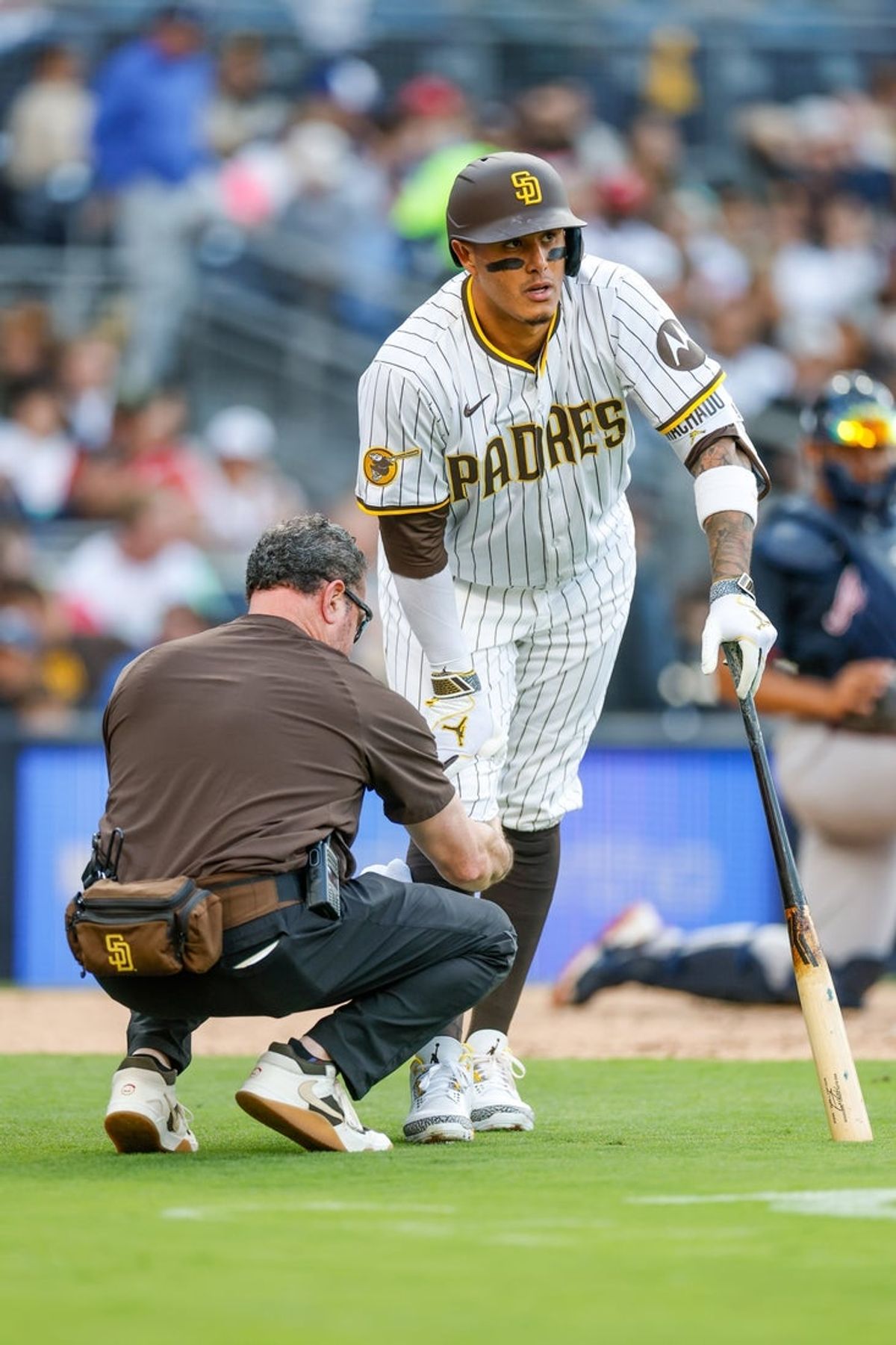 Mar 29, 2025; San Diego, California, USA;  San Diego Padres trainer works with San Diego Padres third baseman Manny Machado (13) during the fourth inning against the Atlanta Braves at Petco Park. Mandatory Credit: David Frerker-Imagn Images