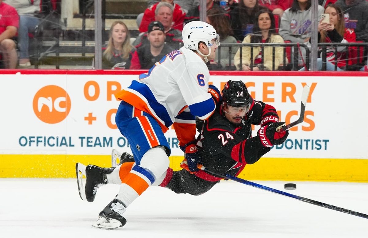 Mar 30, 2025; Raleigh, North Carolina, USA;  Carolina Hurricanes center Seth Jarvis (24) gets the shot away against New York Islanders defenseman Ryan Pulock (6) during the first period at Lenovo Center. Mandatory Credit: James Guillory-Imagn Images