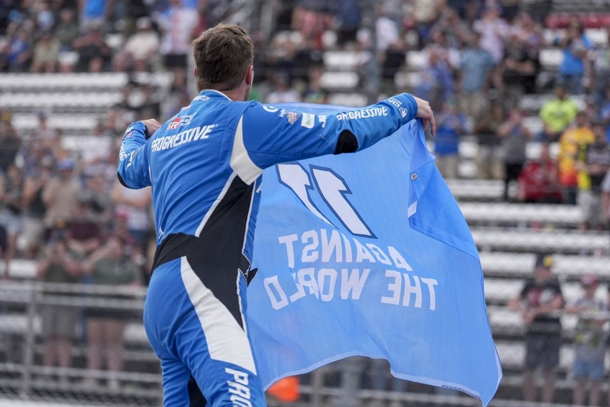Mar 30, 2025; Martinsville, Virginia, USA; NASCAR Cup Series driver Denny Hamlin (11) holds a flag reading “11 Against the World” after his win during the Cook Out 400 at Martinsville Speedway. Mandatory Credit: Jim Dedmon-Imagn Images