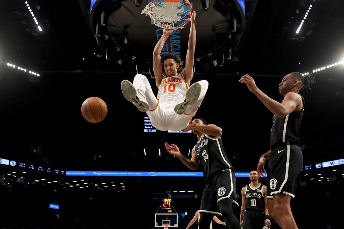 Apr 10, 2025; Brooklyn, New York, USA; Atlanta Hawks forward Zaccharie Risacher (10) hangs on the rim after a dunk against Brooklyn Nets center Nic Claxton (33) and forward Tosan Evbuomwan (12) during the second quarter at Barclays Center. Mandatory Credit: Brad Penner-Imagn Images