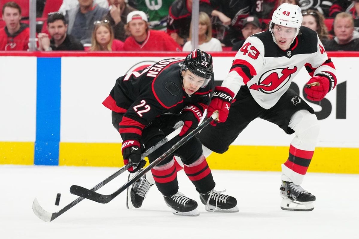 Apr 20, 2025; Raleigh, North Carolina, USA; Carolina Hurricanes center Logan Stankoven (22) battles for the puck against New Jersey Devils defenseman Luke Hughes (43) during the third period of game one of the first round of the 2025 Stanley Cup Playoffs at Lenovo Center. Mandatory Credit: James Guillory-Imagn Images