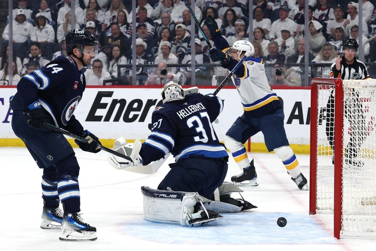 Apr 21, 2025; Winnipeg, Manitoba, CAN; St. Louis Blues right wing Jimmy Snuggerud (21) (not shown) score on Winnipeg Jets goaltender Connor Hellebuyck (37) as teammate St. Louis Blues center Robert Thomas (18) celebrates in the first period in game two of the first round of the 2025 Stanley Cup Playoffs at Canada Life Centre. Mandatory Credit: James Carey Lauder-Imagn Images