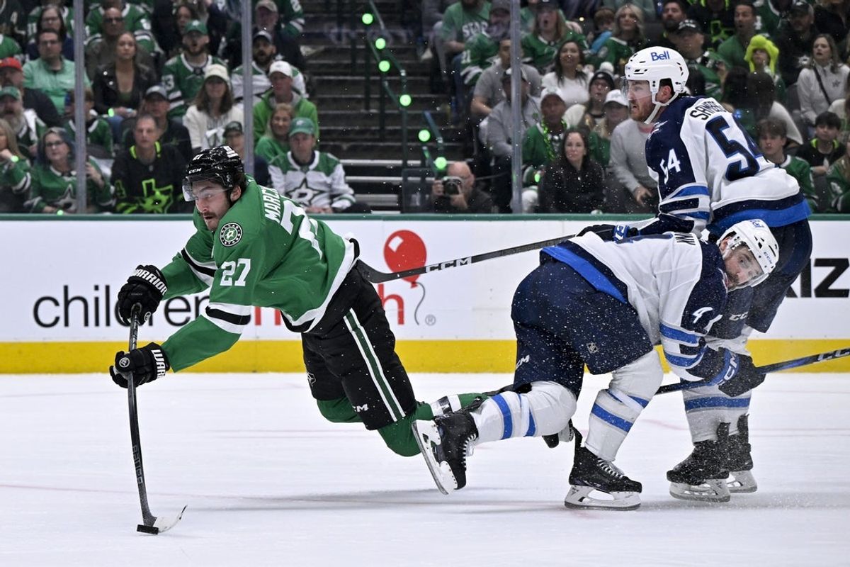 May 11, 2025; Dallas, Texas, USA; Dallas Stars left wing Mason Marchment (27) is tripped up as he shoots the puck past Winnipeg Jets defenseman Neal Pionk (4) and defenseman Dylan Samberg (54) during the second period in Game 3 of the second round of the 2025 Stanley Cup Playoffs at American Airlines Center. Mandatory Credit: Jerome Miron-Imagn Images