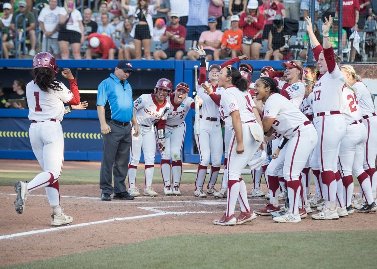 Jun 1, 2025; Oklahoma City, OK, USA;  Oklahoma Sooners players wait on first baseman Cydney Sanders (1) after her two run home run in the third inning against the Oregon Ducks during the NCAA Softball Women's College World Series at Devon Park. Mandatory Credit: Brett Rojo-Imagn Images