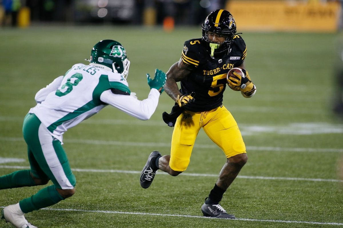 Jun 14, 2025; Hamilton, Ontario, Canada; Hamilton Tiger-Cats running back Greg Bell (5) tries to avoid a tackle from Saskatchewan Roughriders defensive back Marcus Sayles (8) at Hamilton Stadium. Mandatory Credit: John E. Sokolowski-Imagn Images