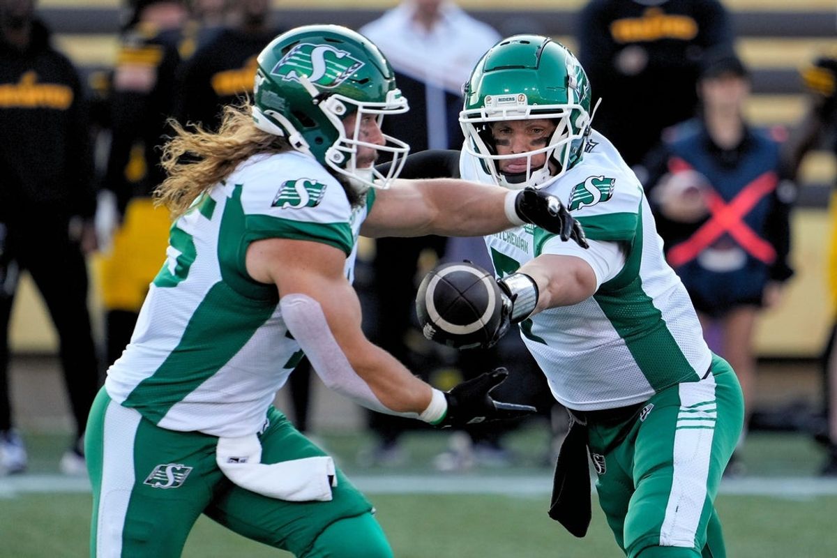 Jun 14, 2025; Hamilton, Ontario, Canada; Saskatchewan Roughriders quarterback Trevor Harris (7) hands the ball off to running back A.J. Ouellette (45) during a game against the Hamilton Tiger-Cats at Hamilton Stadium. Mandatory Credit: John E. Sokolowski-Imagn Images