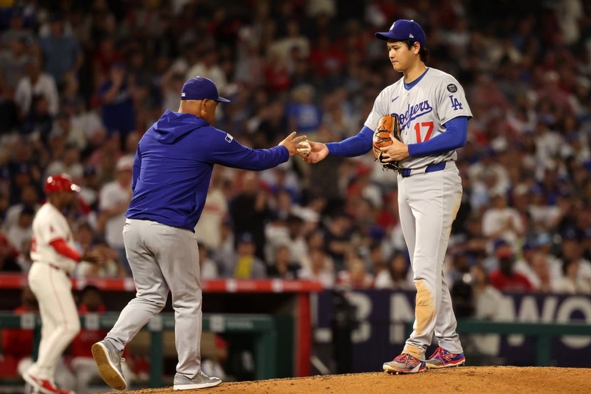 Aug 13, 2025; Anaheim, California, USA;  Los Angeles Dodgers two-way player Shohei Ohtani (17) hands the ball to manager Dave Roberts (30, left) during the fifth inning against the Los Angeles Angels at Angel Stadium. Mandatory Credit: Kiyoshi Mio-Imagn Images