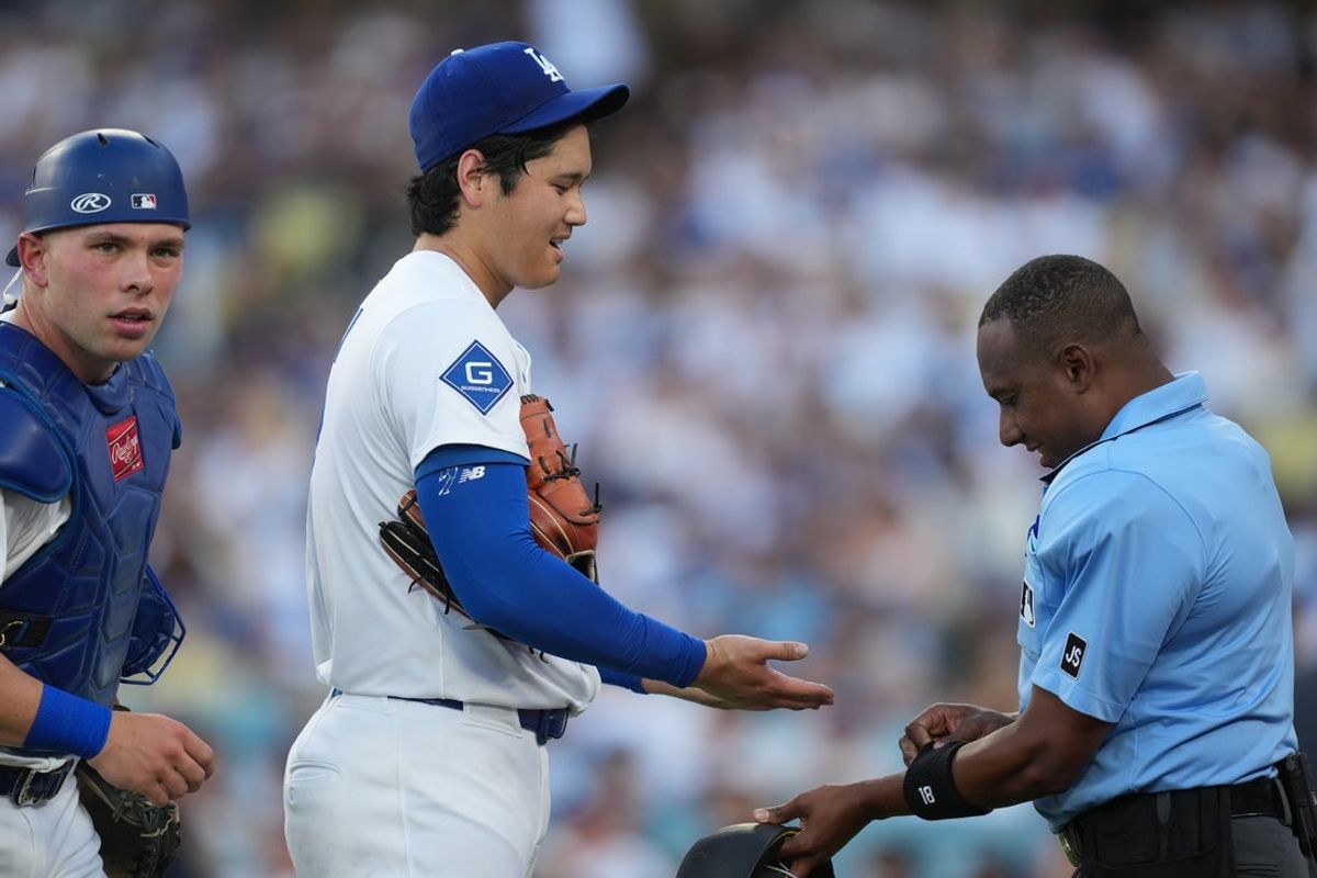 Aug 27, 2025; Los Angeles, California, USA; Umpire Ramon De Jesus (18) checks the hands of Los Angeles Dodgers starting pitcher Shohei Ohtani (17) in the first inning against the Cincinnati Reds at Dodger Stadium. Mandatory Credit: Kirby Lee-Imagn Images