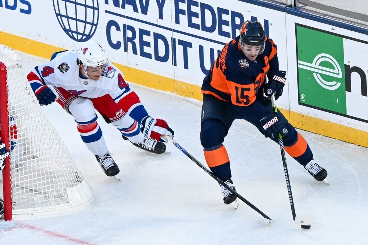 Feb 18, 2024; East Rutherford, New Jersey, USA;  New York Islanders right wing Cal Clutterbuck (15) skates with the puck defended by New York Rangers defenseman Braden Schneider (4) during the first period in a Stadium Series ice hockey game at MetLife Stadium.