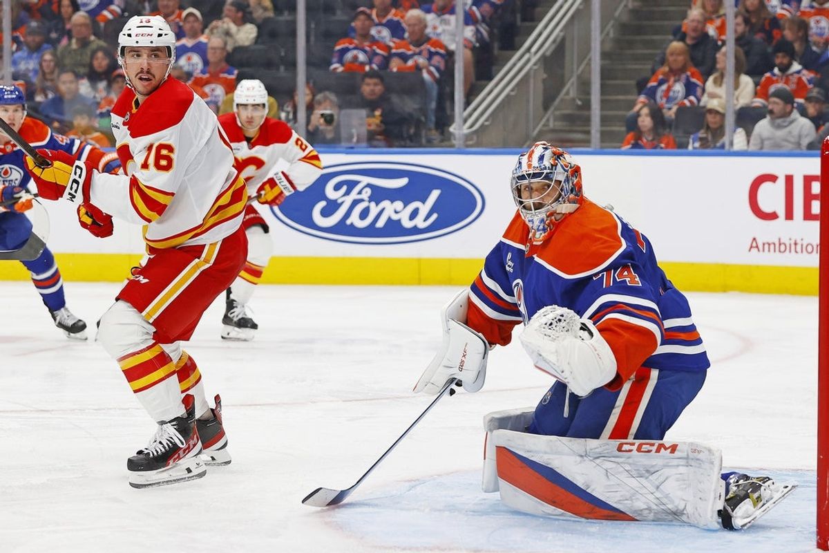Oct 8, 2025; Edmonton, Alberta, CAN; Calgary Flames forward Morgan Frost (16) and Edmonton Oilers goaltender Stuart Skinner (74) look for a loose puck during the second period at Rogers Place. Mandatory Credit: Perry Nelson-Imagn Images