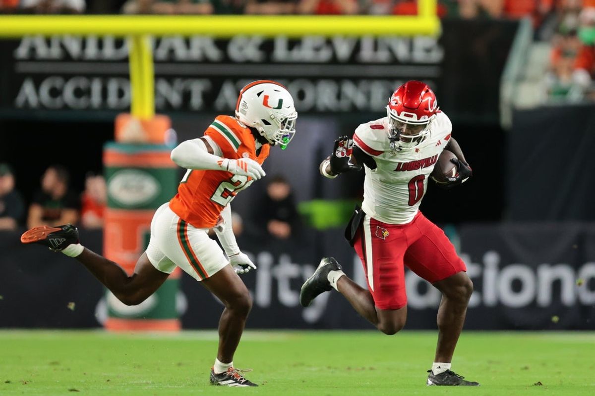 Oct 17, 2025; Miami Gardens, Florida, USA; Louisville Cardinals wide receiver Chris Bell (0) carries the football against Miami Hurricanes defensive back Jr. Romanas Frederique (29) during the second quarter at Hard Rock Stadium. Mandatory Credit: Sam Navarro-Imagn Images