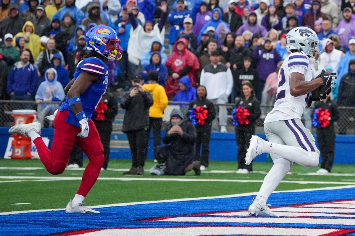 Oct 25, 2025; Lawrence, Kansas, USA; Kansas State Wildcats wide receiver Jaron Tibbs (12) scores a touchdown as Kansas Jayhawks defensive back Austin Alexander (0) chases during the first half of the game at David Booth Kansas Memorial Stadium. Mandatory Credit: Denny Medley-Imagn Images