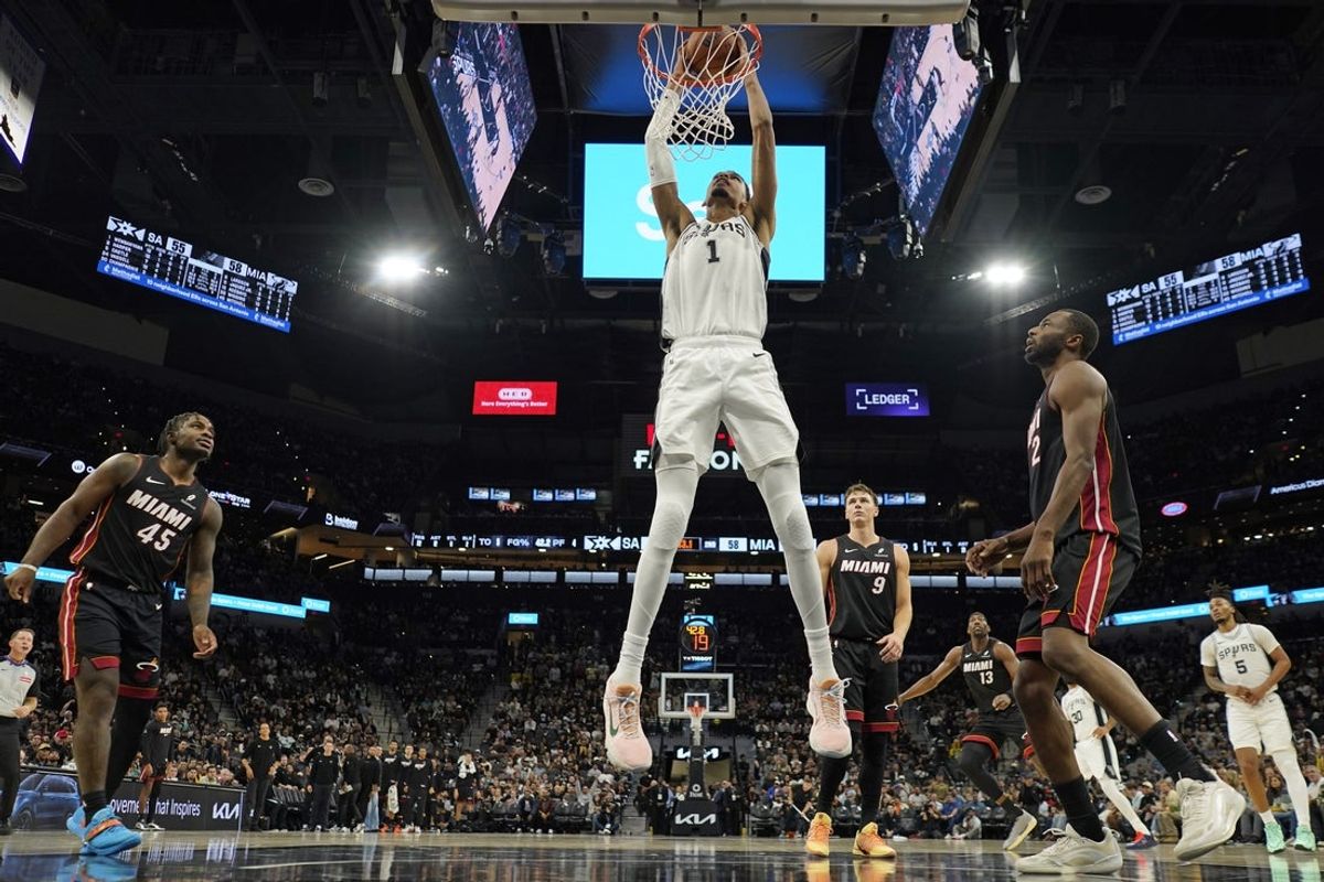 Oct 30, 2025; San Antonio, Texas, USA; San Antonio Spurs forward Victor Wembanyama (1) dunks over Miami Heat guard Davion Mitchell (45) and forward Andrew Wiggins (22) during the first half at Frost Bank Center. Mandatory Credit: Scott Wachter-Imagn Images