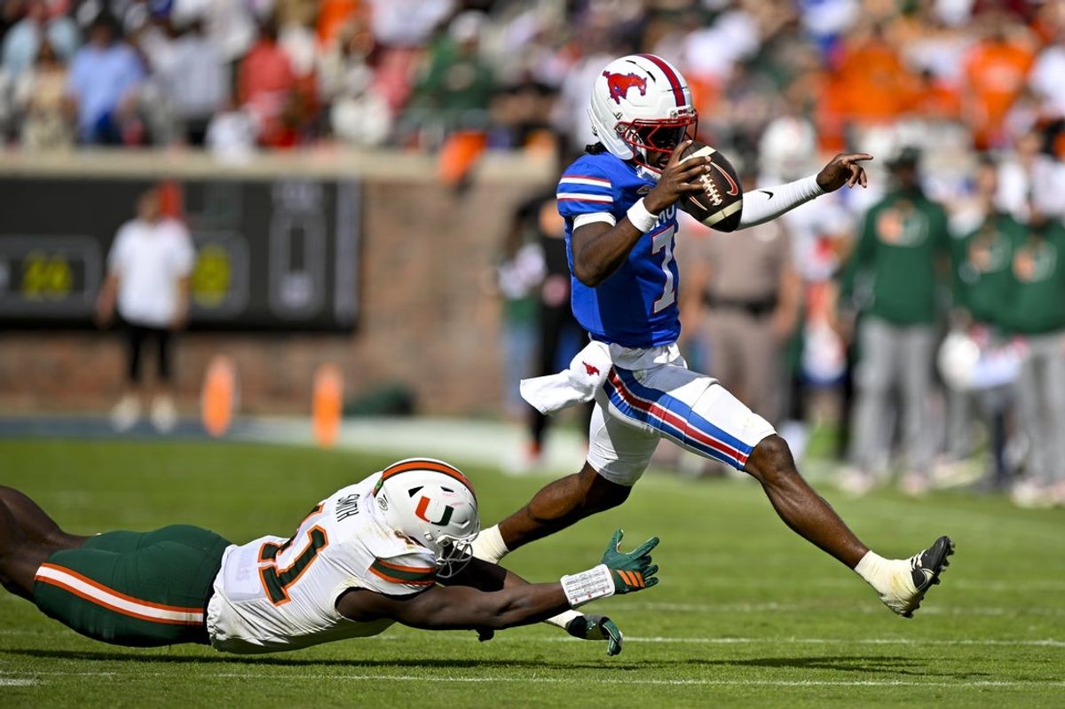 Nov 1, 2025; Dallas, Texas, USA;  SMU Mustangs quarterback Kevin Jennings (7) leaps over Miami Hurricanes defensive lineman David Blay (11) during the second half at Gerald J. Ford Stadium. Mandatory Credit: Jerome Miron-Imagn Images