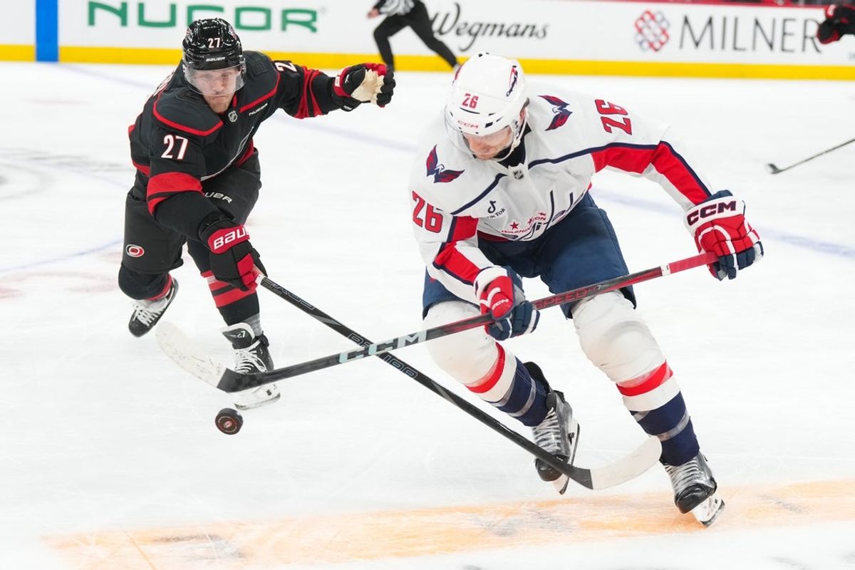 Nov 11, 2025; Raleigh, North Carolina, USA;  Washington Capitals center Nic Dowd (26) tries to chip the puck past Carolina Hurricanes left wing Nikolaj Ehlers (27) during the first period at Lenovo Center. Mandatory Credit: James Guillory-Imagn Images